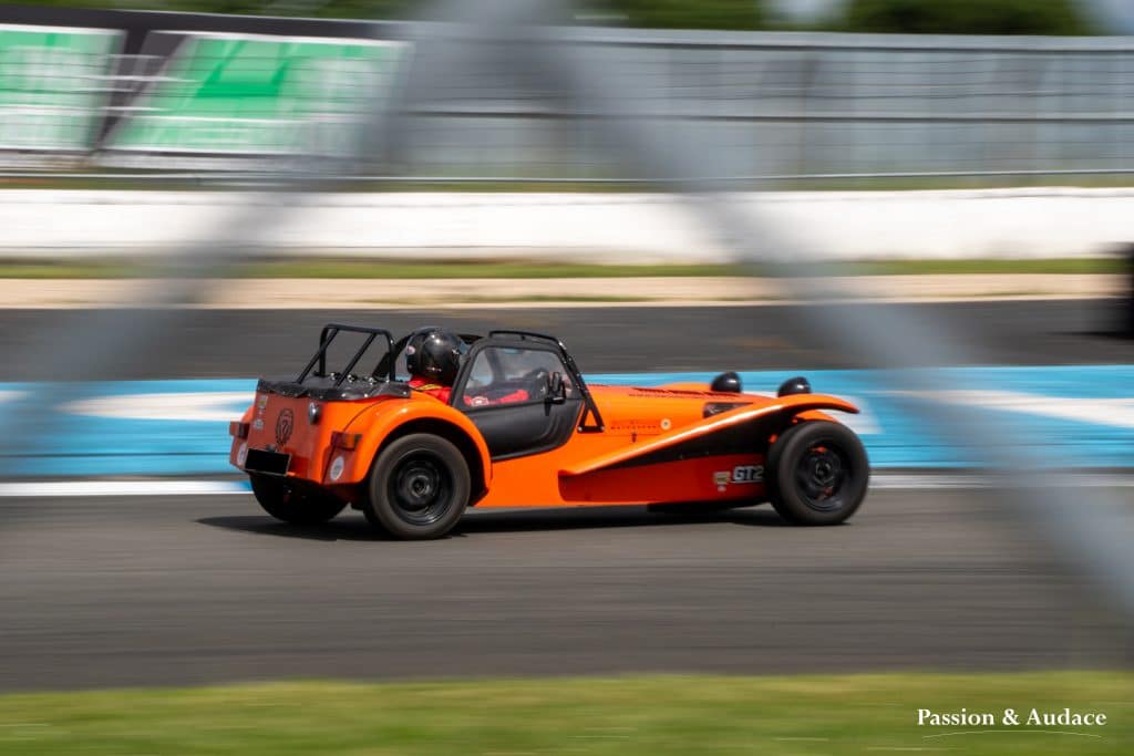 Pilote de monoplace en pleine course sur le circuit d'Albi vu entre les croisillons d'un grillage