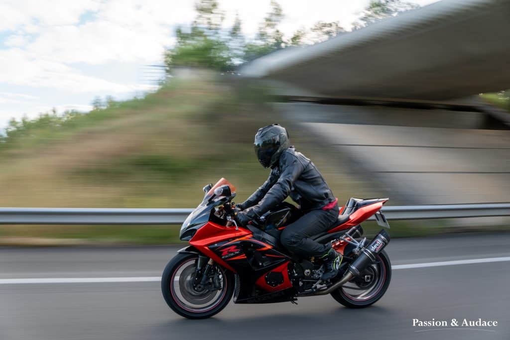 Motard sur sa moto Suzuki GSXR orange et noir sur l'autoroute avec un effet de vitesse à l'arrière-plan
