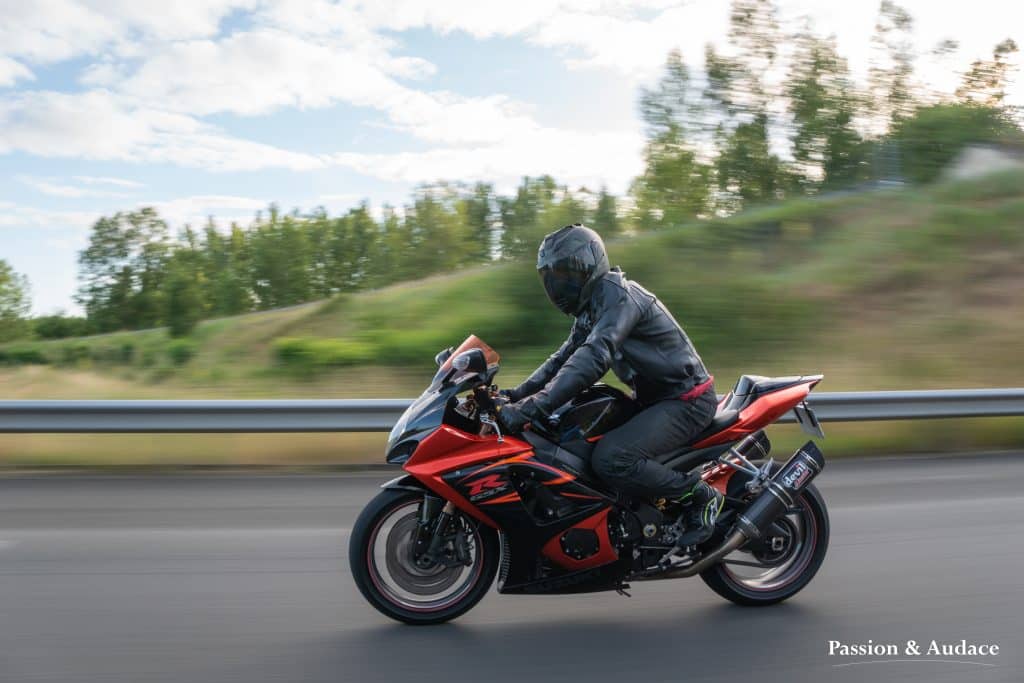 Motard sur sa moto Suzuki GSXR orange et noir sur l'autoroute avec un effet de vitesse à l'arrière-plan et regardant vers l'objectif photo
