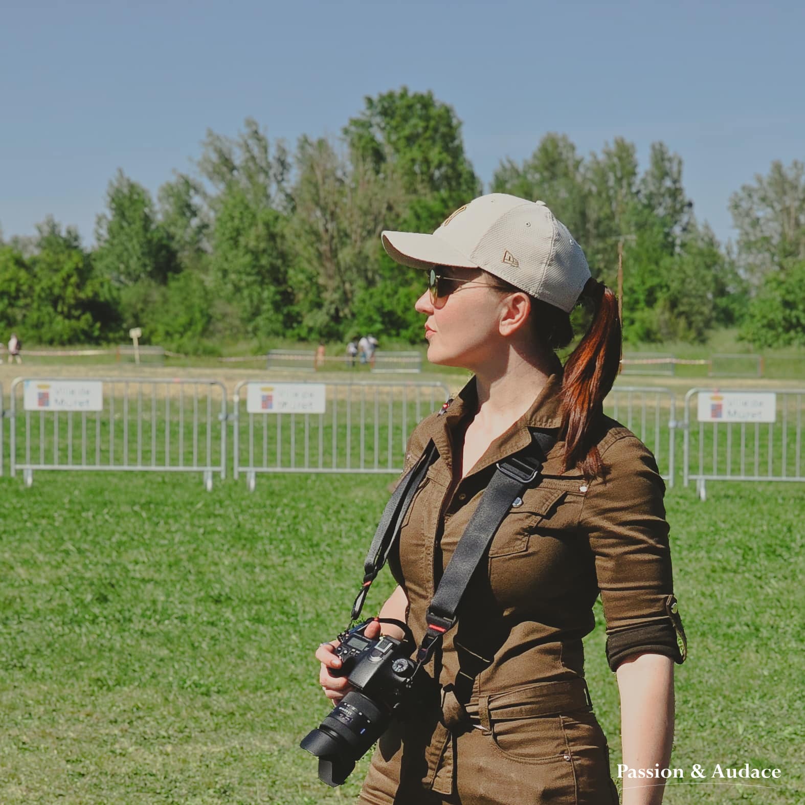 Photographie de profil d'une photographe en combinaison kaki tenant son appareil photo dans la main
