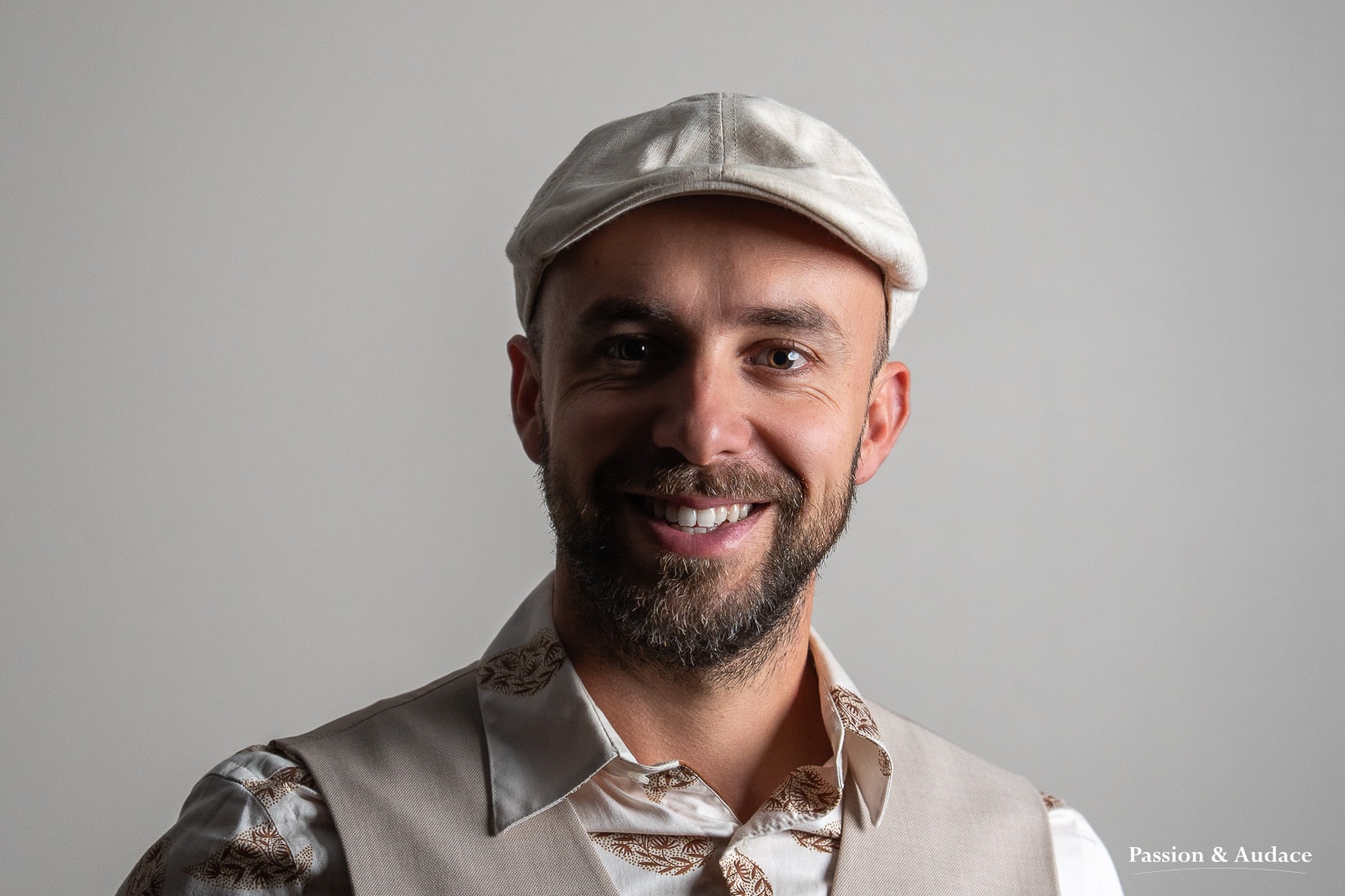 Photographie de portrait d'un professionnel souriant en tenue corporate avec une chemise et un gilet de costume beige et un béret crème sur la tête