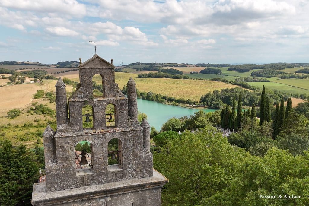 Photographie aérienne du clocher d'une église dans la végétation verdoyante. Étendue de champs à l'arrière-plan.