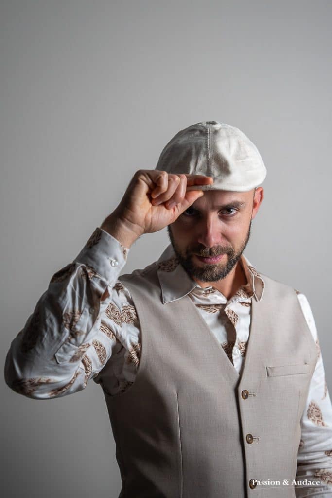 Photographie de portrait d'un homme en tenue corporate avec une chemise et un gilet de costume beige et un béret crème sur la tête regardant vers l'objectif