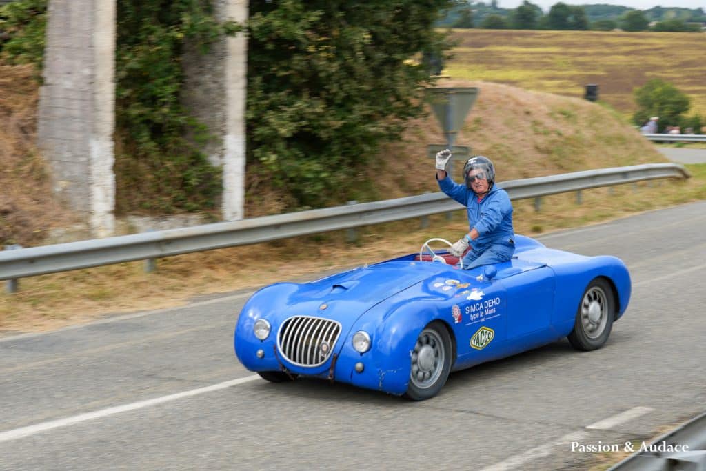 Photographie d'un homme debout dans son véhicule bleu en train de lever le bras tout en faisant la course sur le circuit de Cadours Laréole