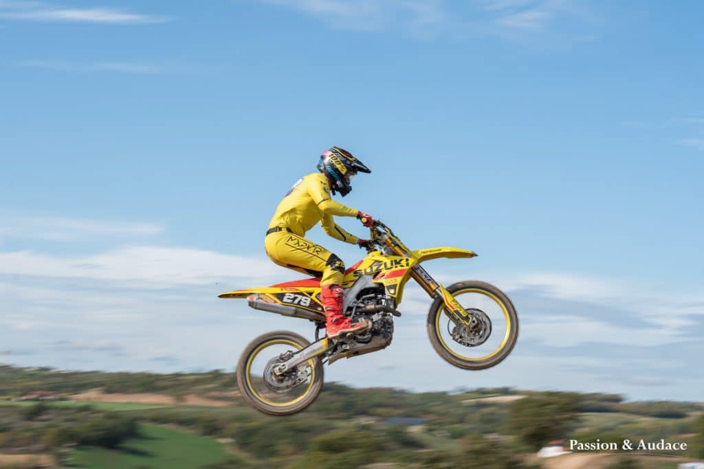 Photographie d'un pilote de cross en plein parcours avec un effet de filé de vitesse en train de décoller dans les airs