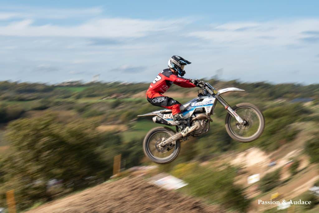 Photographie d'un pilote de cross en plein parcours avec un effet de filé de vitesse en train de décoller dans les airs