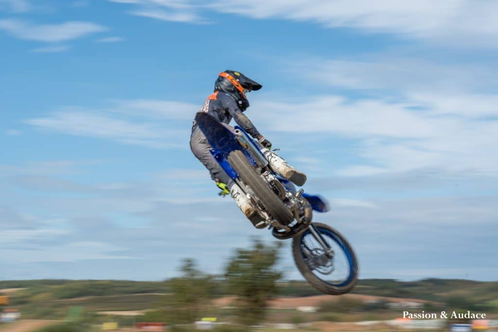 Photographie d'un pilote de cross en plein parcours avec un effet de filé de vitesse en train de faire une figure acrobatique en plein vol