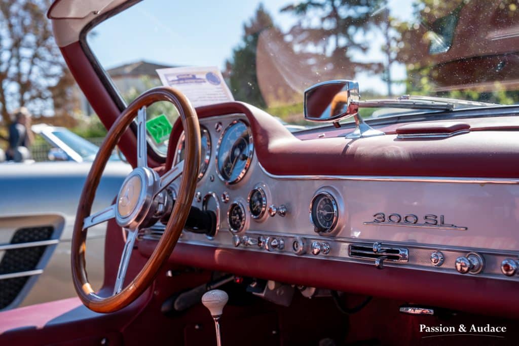 Photographie du tableau de bord d'une Mercedes 300SL. Photo prise depuis la porte passager. Volant bois et cuir rouge.