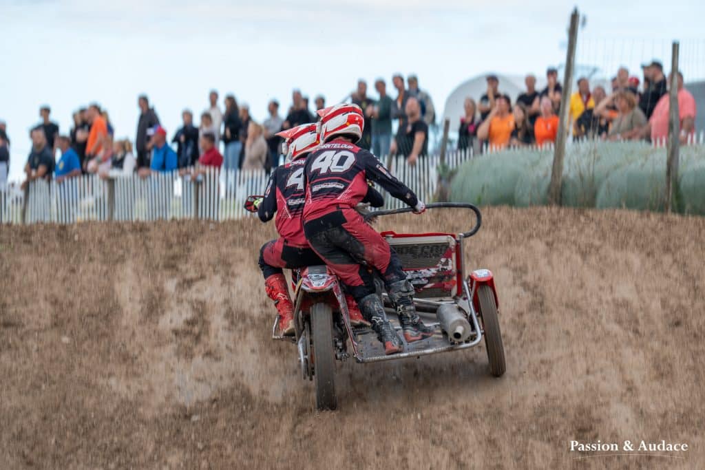 Photographie d'un pilote de sidecar cross avec son copilote en plein virage d'une course avec la foule en arrière-plan